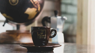 Tazzina caffè espresso Filicori Zecchini Centenario, con caffettiera Moka e mappamondo sullo sfondo.