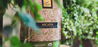 Detalle de una bolsa de granos de café orgánico Arcadia con plantas al fondo.