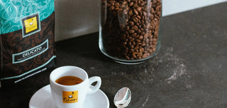 Tasse Espresso von Filicori Zecchini, mit einer Tüte Delicato-Mischung und einem Glas mit Kaffeebohnen im Hintergrund.