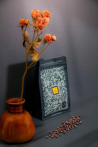 Sacchetto da 250g di caffè specialty - ramo di rose essiccate in vaso di ceramica - chicchi di caffè sparsi.