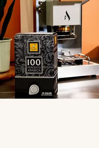100 Percento Arabica in einer Schachtel mit 18 Kaffeepads und Aroma-Pad-Maschine im Hintergrund.