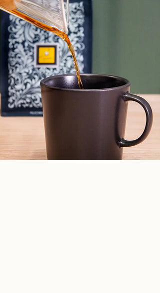 Black mug in the foreground with coffee poured from a Chemex. Specialty Filicori Zecchini bag in the background.